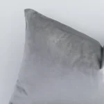 Corner section image showing features of rectangle silver cushion that has a solid colour motif on its velvet fabric.