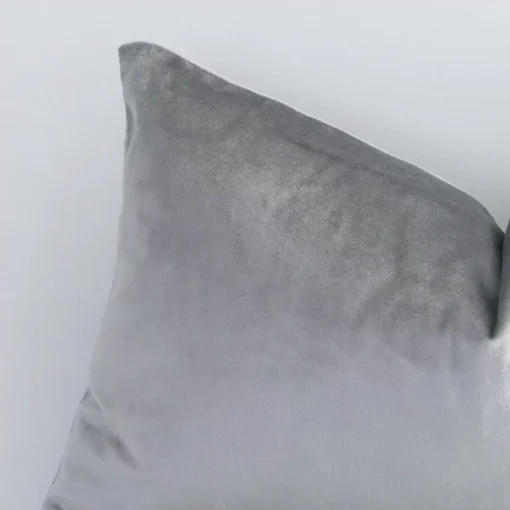 Corner section image showing features of rectangle silver cushion that has a solid colour motif on its velvet fabric.