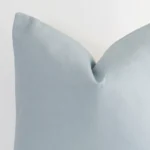 A macro image of the top left corner of this solid-coloured linen cushion. It is possible to see the finer detail of the large size and soft teal colour.