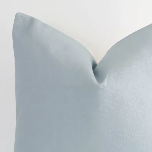 A macro image of the top left corner of this solid-coloured linen cushion. It is possible to see the finer detail of the large size and soft teal colour.