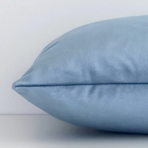 A rectangle stone blue cushion cover laying flat. This viewpoint highlights the solid colour style and velvet fabric from a side position.