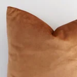 Close up image of top corner of this solid-coloured terracotta cushion. This shows the velvet fabric and square shape up close.