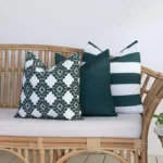 A rattan seat in front of a white wall is styled with a set of 3 Byron green outdoor cushions.