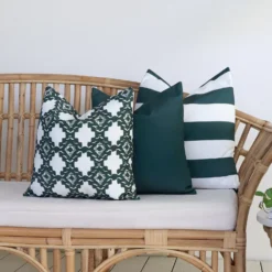 A rattan seat in front of a white wall is styled with a set of 3 Byron green outdoor cushions.