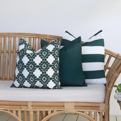 A rattan seat in front of a white wall is styled with a set of 3 Byron green outdoor cushions.