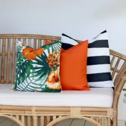 A set of 3 Byron orange cushions are on a rattan seat in the outdoor area.