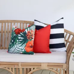 A rattan seat next to a green plant has 3 outdoor cushions from the Byron collection on it.