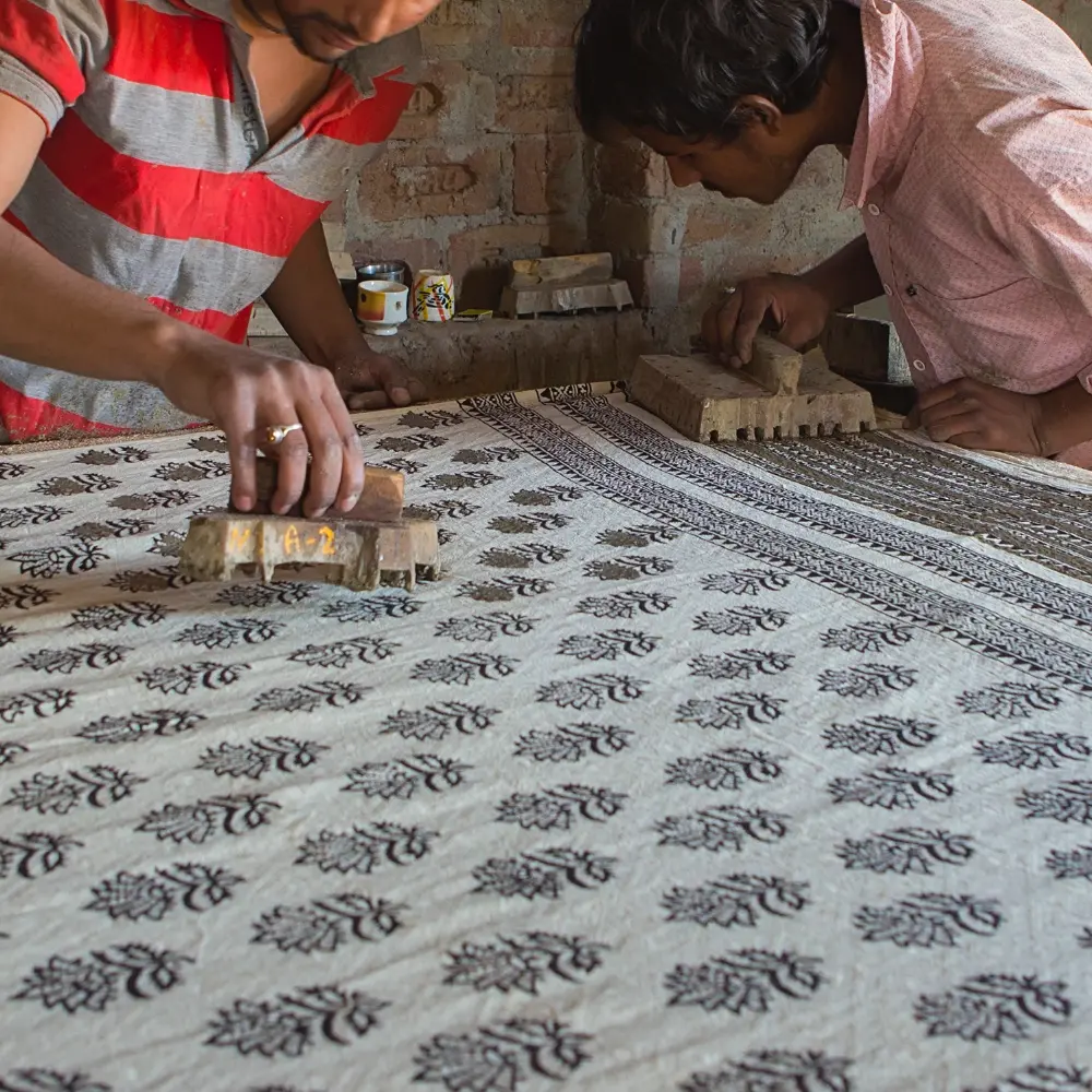 Two artisans are creating a fabric using traditional Indian wooden block printing technique.
