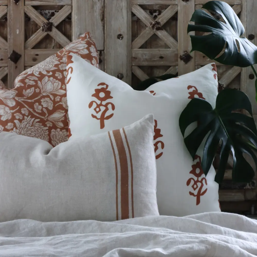 An elegant display of linen cushions in front of an ornate wooden door and plant.