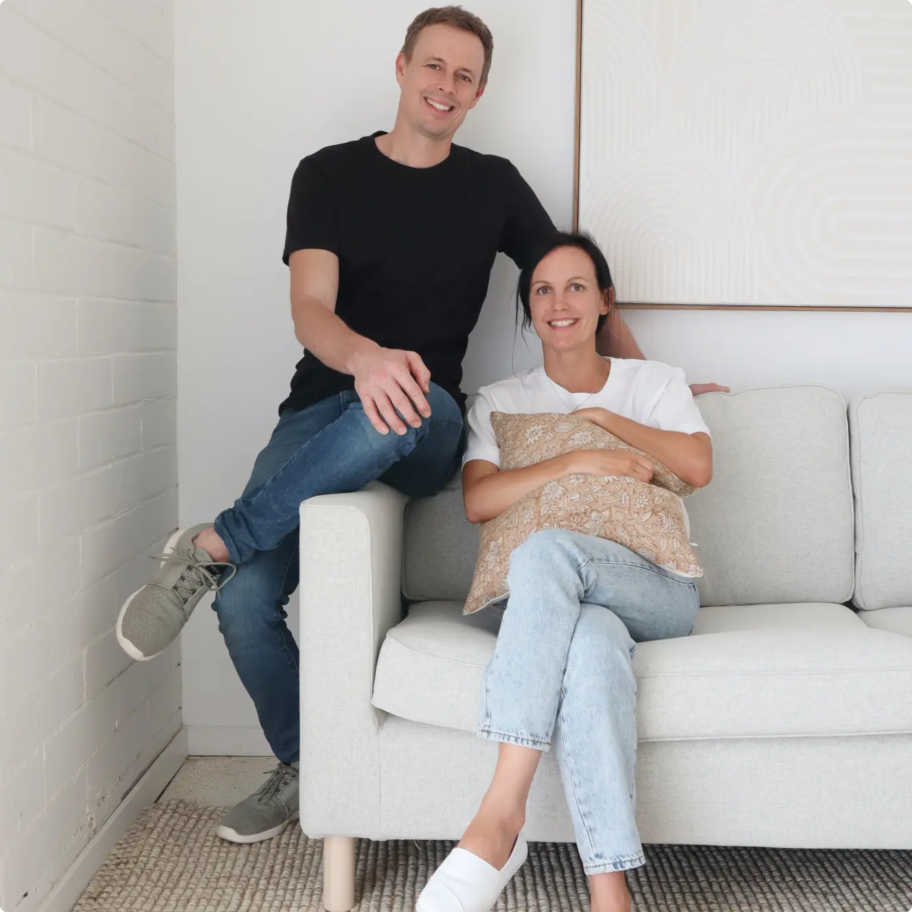 Two founders sitting on a light sofa with wall art in background.