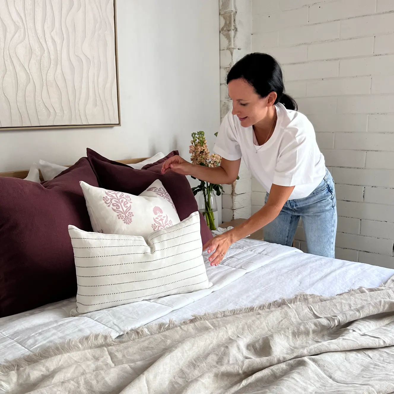 A lady styling some cushions in a light filled and bright bedroom.