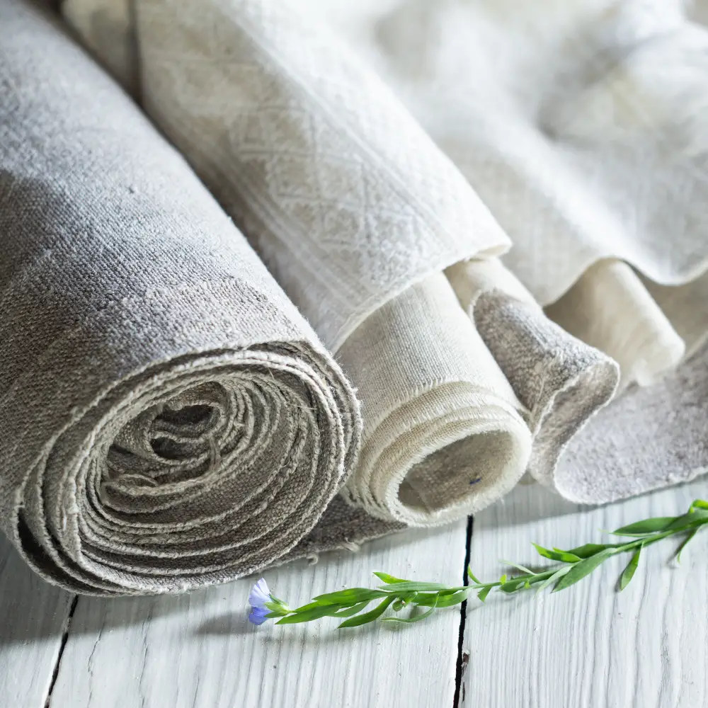 Some linen fabric rolls are shown side by side with a flax plant that has a flower.