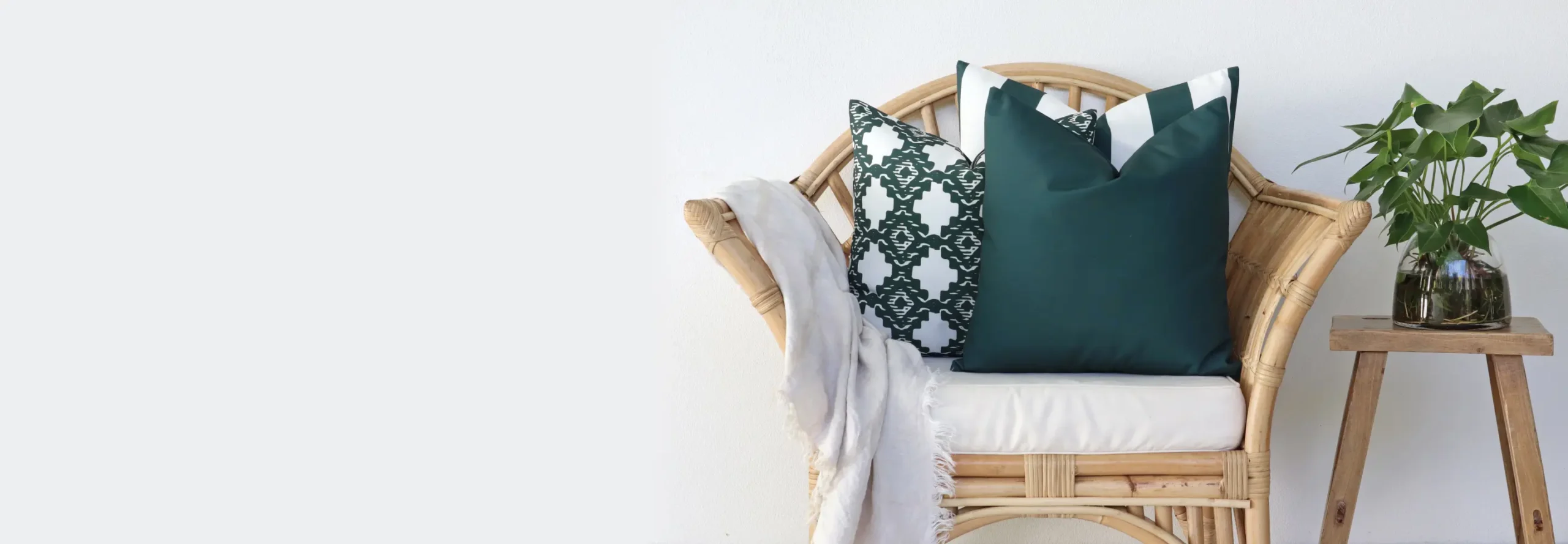 Outdoor cushions arranged on a chair with a light coloured throw and a plant nearby.