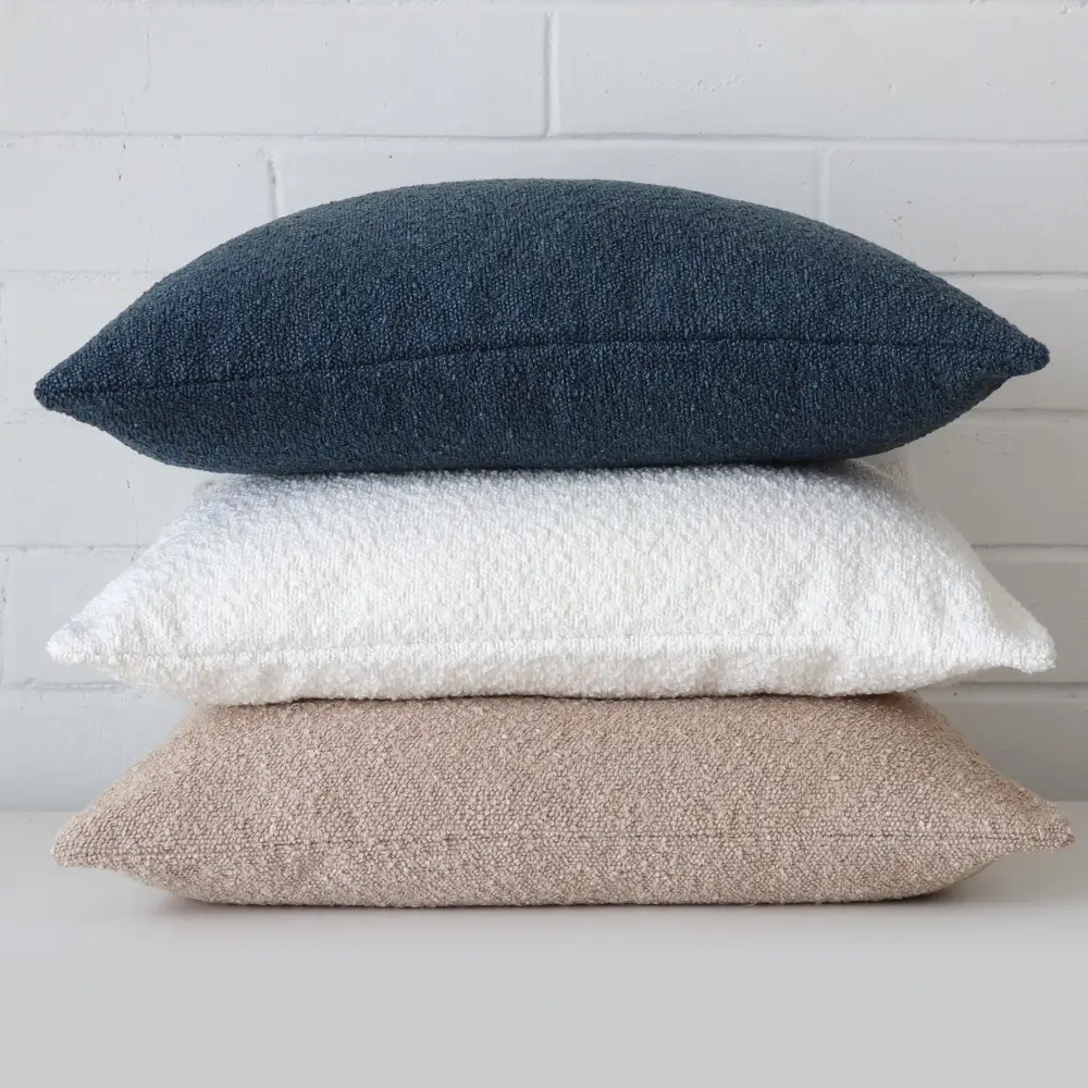 A pile of three boucle cushions stacked upon each other showing texture across three colours.