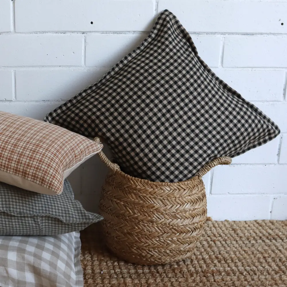 A premium Lithuanian linen designer cushion sits in a woven basket next to other designs in a stack.