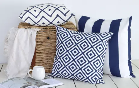 A scene showing blue outdoor cushions laying against a basket with a throw and book.