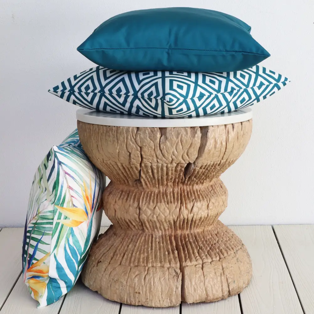 A small wooden round table with outdoor cushions stacked upon it.