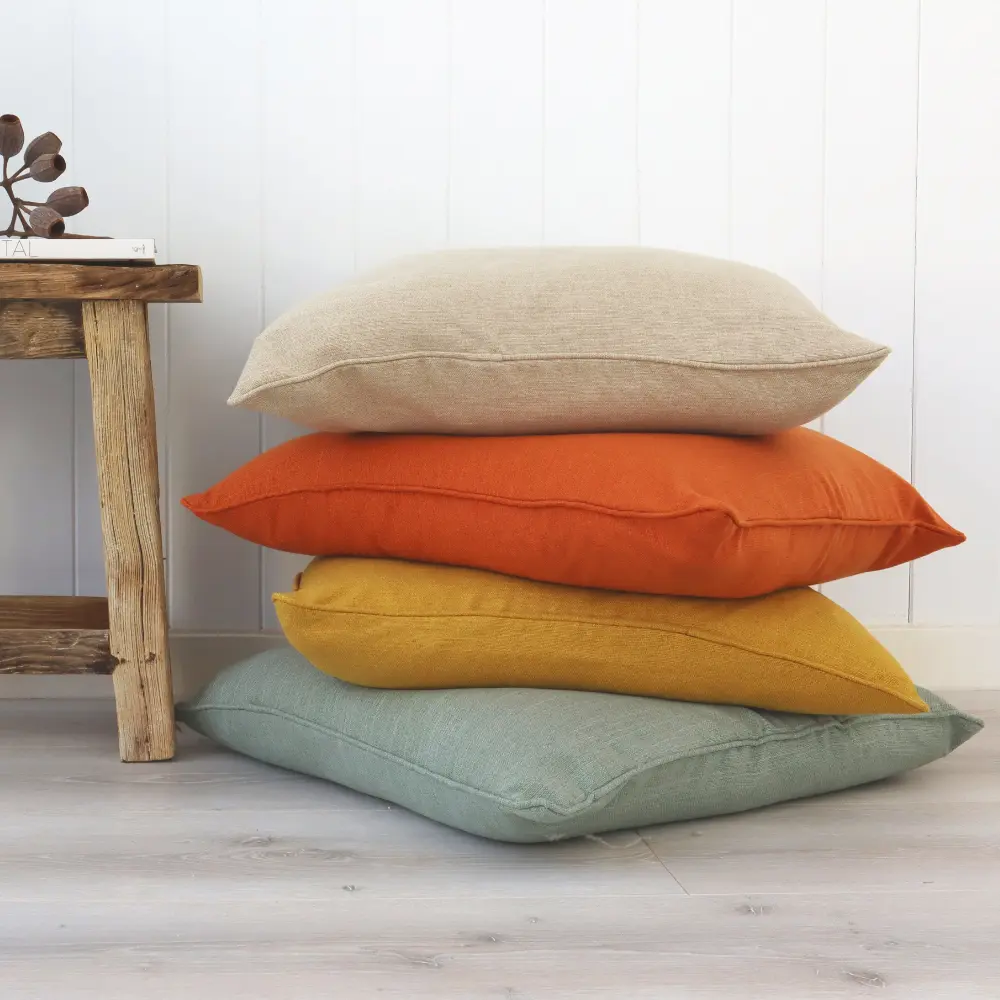 A stack of colourful polyester cushions against a wall and next to a small table.