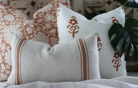 A styled group of classic cushions sit on top of a throw with wood in the background.
