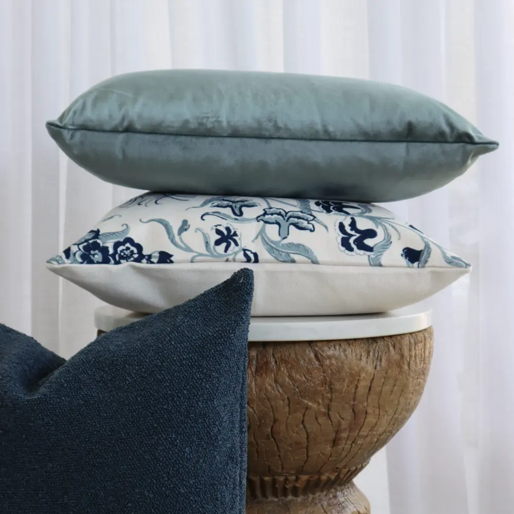 A small table hosts a collection of designs with a velvet cushion sitting on top.
