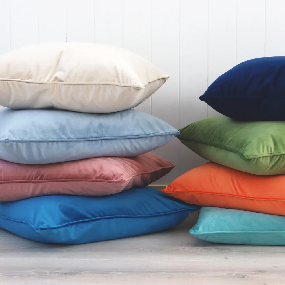Two stacks of velvet cushions shown with a wide range of bold colours.