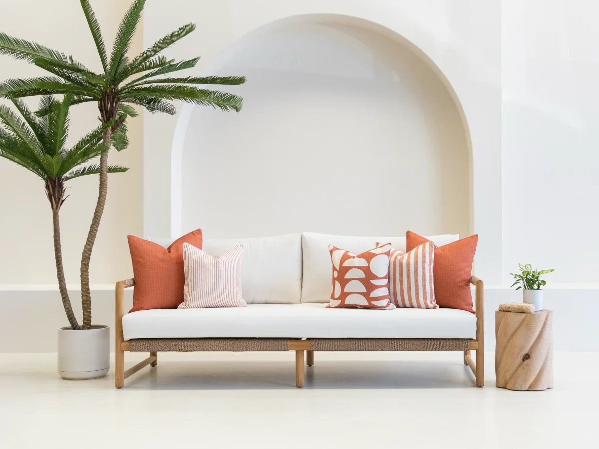 A 3 seater outdoor sofa with 5 rust coloured outdoor cushions on it.