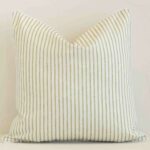 An attractive striped outdoor cushion in front of a white brick wall. It has a square shape and is sage in colour.