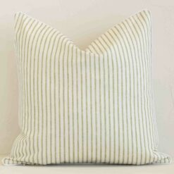 An attractive striped outdoor cushion in front of a white brick wall. It has a square shape and is sage in colour.