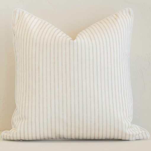 White wall with a stripe sand cushion laying against it. It has a distinctive outdoor fabric and has a square shape.