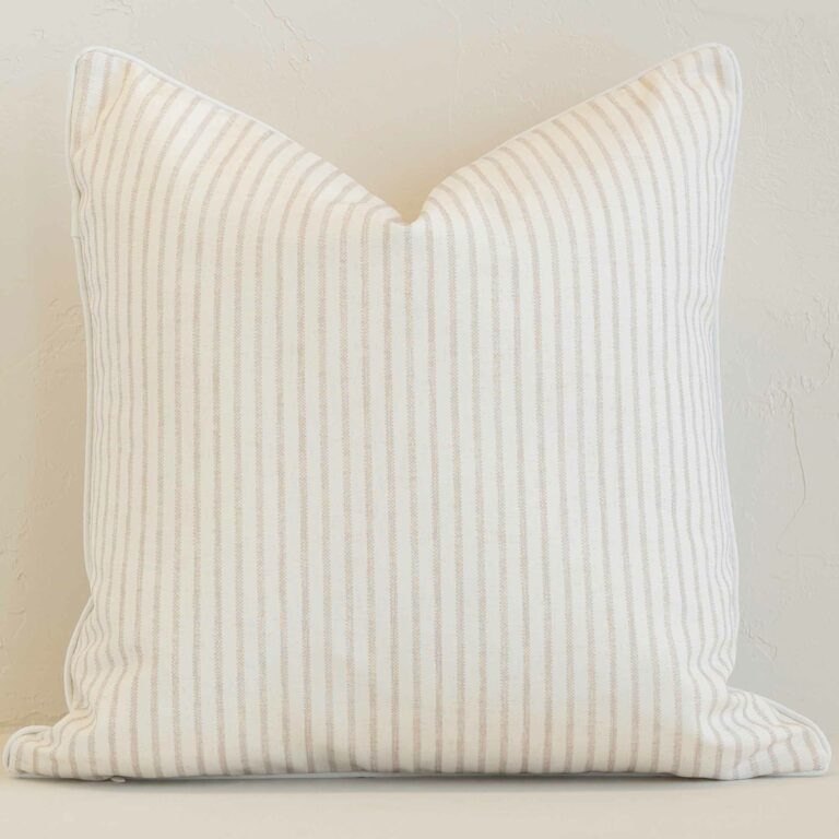 White wall with a stripe sand cushion laying against it. It has a distinctive outdoor fabric and has a square shape.