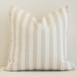 Square stripe cushion cover in sand colour sitting upright in front of a brick wall. It has been made from a quality outdoor material.