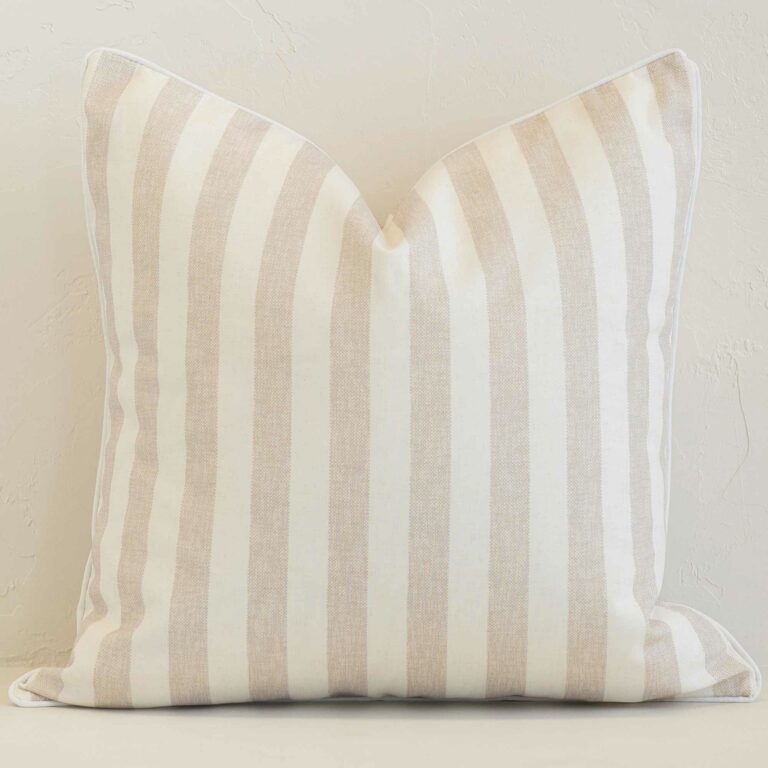 Square stripe cushion cover in sand colour sitting upright in front of a brick wall. It has been made from a quality outdoor material.