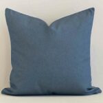 Outdoor large cushion with a solid- coloured design in an upright position against a white brick wall.