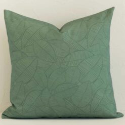 A lovely large green cushion cover arranged in front of a white wall. The floral style complements the outdoor material.