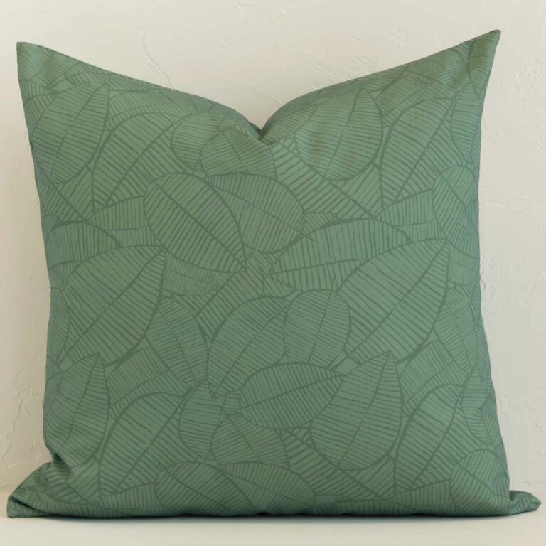 A lovely large green cushion cover arranged in front of a white wall. The floral style complements the outdoor material.
