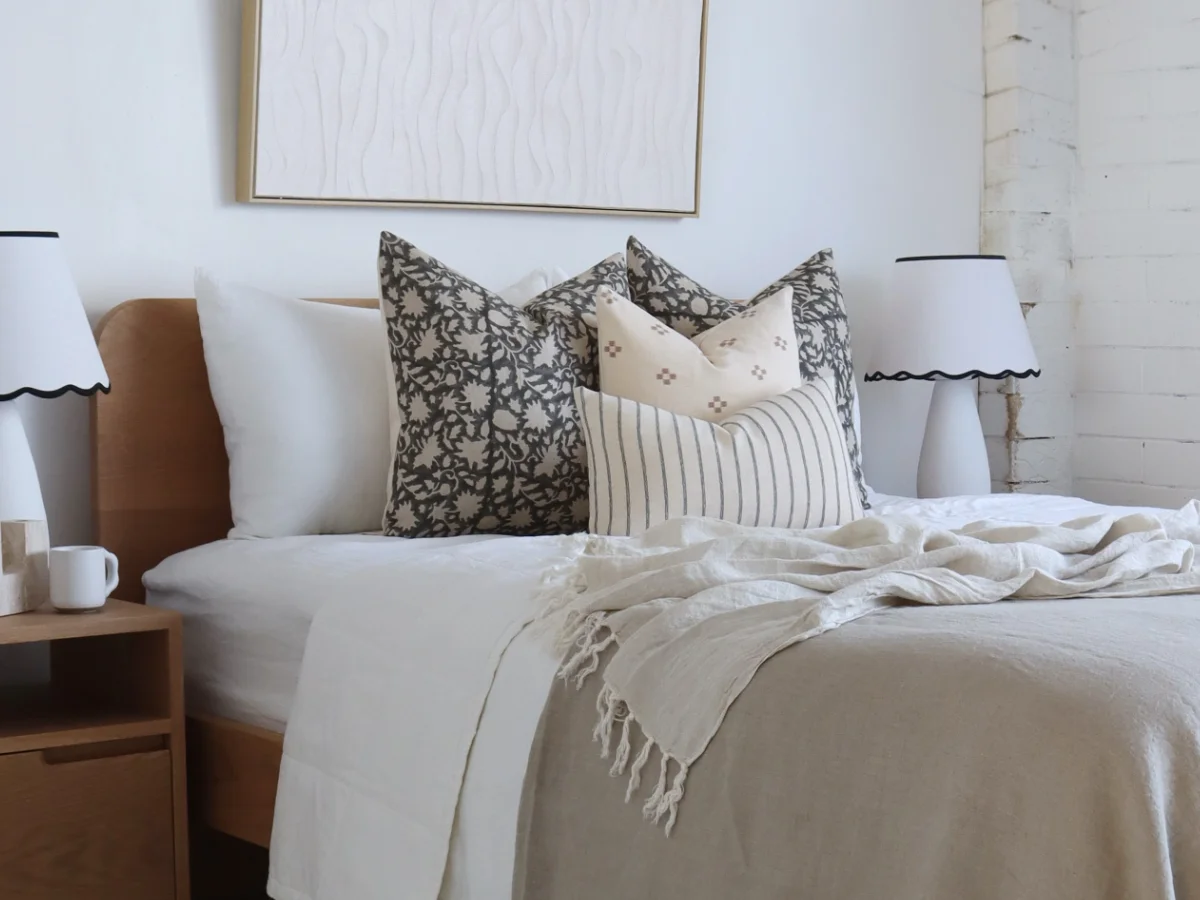 A bedroom is shown with a bed styled using cushions with designer fabrics on top of a neutral bedspread.