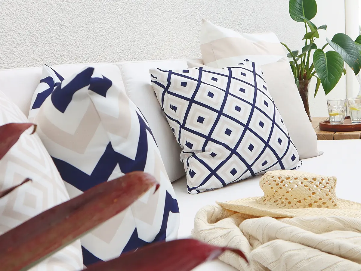 Several beige and navy outdoor cushions styled on light coloured outdoor modular seating.