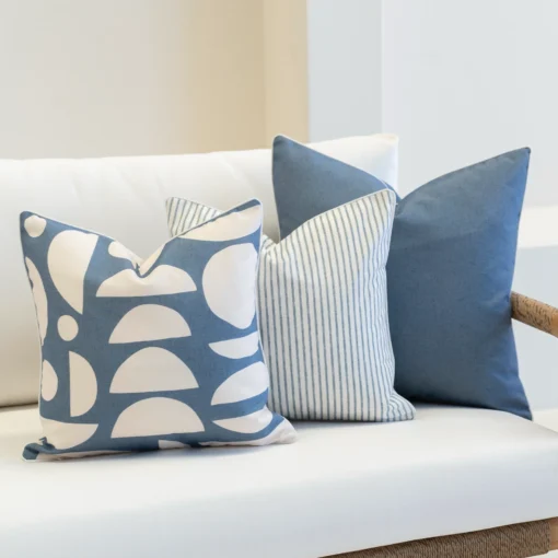 A set of 3 pacific blue coloured outdoor cushions are sitting in the corner of a white sofa.