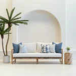 A set of 5 pacific blue outdoor cushions sitting on a wooden sofa in an airy white living room.