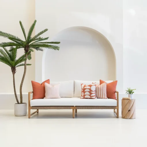 A white outdoor living space featuring a wooden sofa styled with a set of five Pacific Rust outdoor cushions.