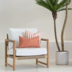 A wooden single-seater sofa styled with two rust outdoor cushions.