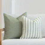 2 outdoor cushions in pacific sage colour displayed on a white sofa's corner.