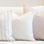 A set of 3 outdoor couch cushions in pacific sand colour are displayed on a white couch.