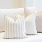 A set of 3 outdoor cushions in a pacific sand colour are neatly arranged on a white sofa.