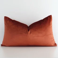 Bold rectangle rust cushion positioned in front of white wall. It has an elegant velvet material.