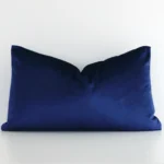 Royal blue cushion cover in front of a white wall. It has a rectangle size and is made from a velvet material.