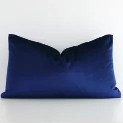 Royal blue cushion cover in front of a white wall. It has a rectangle size and is made from a velvet material.