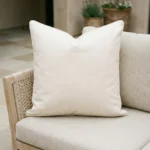 Cream waterproof cushion with white piping on woven outdoor armchair.