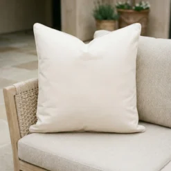 Cream waterproof cushion with white piping on woven outdoor armchair.