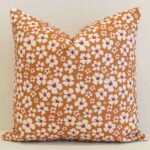 Ditsy floral cushion cover with delicate white blossoms on a warm ochre base for a fresh, inviting look.